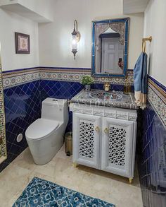 a white toilet sitting next to a sink in a bathroom under a blue and white mirror