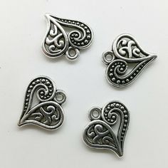 four silver tone heart charms with filigrees and swirl designs on white background