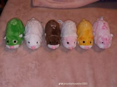 five small stuffed animals lined up in a row on a pink blanket with someone's hand behind them