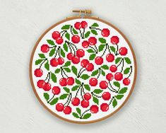 a cross stitch pattern with cherries and leaves on a white wall behind a wooden frame