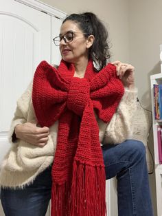 a woman sitting in a chair wearing a red knitted scarf with fringes on it