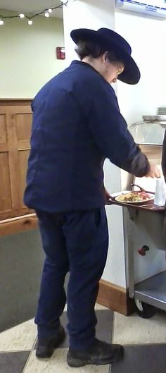 two people standing in front of a counter with food on it and one person wearing a hat