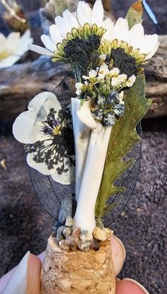 a hand holding a vase with white flowers and leaves in it's centerpiece