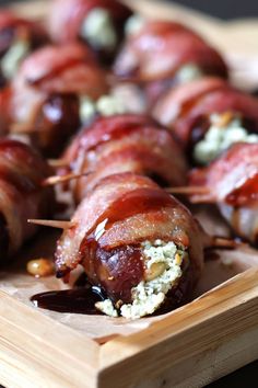 bacon wrapped appetizers with cheese and sauce on a wooden tray, ready to be eaten