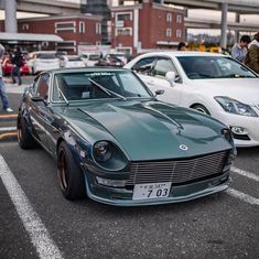 several cars parked in a parking lot with people walking around the area and buildings behind them