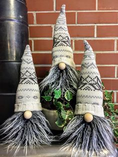 three knitted gnomes sitting on top of a table next to a potted plant