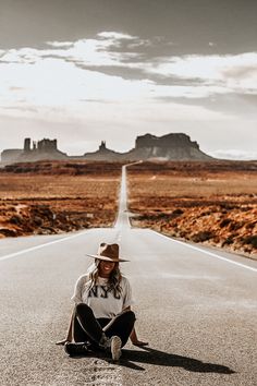 a woman sitting on the side of an empty road