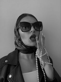 a woman wearing sunglasses and a scarf with pearls on her head is posing for the camera