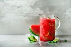 a pitcher filled with watermelon juice next to slices of cucumber and mint