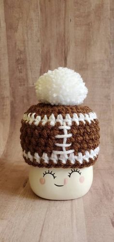 a white cup with a brown and white knitted football hat on it