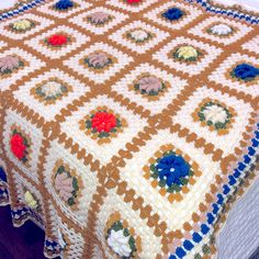 a crocheted blanket on top of a bed with red, white and blue flowers