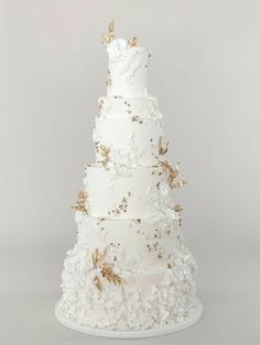 a three tiered white wedding cake with gold leaves and flowers on the bottom layer