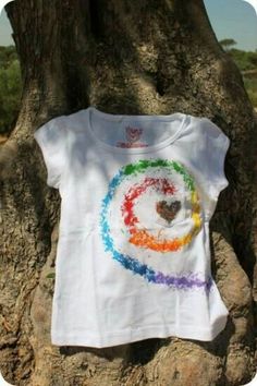 a t - shirt hanging on a tree in front of some rocks and trees with the colors of the rainbow painted on it