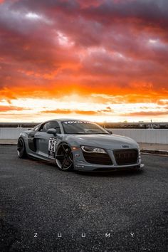 a silver sports car parked in front of a sunset