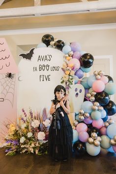 a woman standing in front of a halloween backdrop with balloons and decorations on the wall