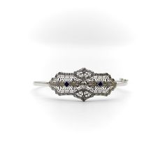 This is part of Chairish’s Fine Jewelry assortment.  A delicate Art Deco bracelet made of 14k white gold with a European cut diamond centre and two French cut sapphires on the side. The centrepiece has a symmetrical design, filled with delicate filagree and a scrolling foliate motif that is detailed and beautifully crafted. The diamond measures 4 mm and has .25 carat weight, it is G/H in colour and VS11 in clarity. The sapphires measure about 2.5 mm and have a well saturated blue tone. The centr Art Deco Diamond Cut Platinum Bracelet, Art Deco Platinum Diamond Cut Bracelet, Exquisite Hand-set Diamond Platinum Bracelet, Exquisite Hand-set Platinum Diamond Bracelet, Exquisite Diamond Cut Platinum Bracelet, Exquisite Platinum Diamond Cut Bracelet, Art Deco Diamond Bracelet In White Gold, Art Deco White Gold Diamond Bracelets, Art Deco White Gold Diamond Cut Bracelet