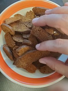 two hands reaching for some bread on an orange and white plate with another hand holding something in it