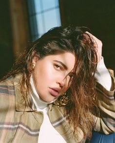 a woman with long hair wearing a plaid jacket and white turtle neck shirt sitting on a blue chair