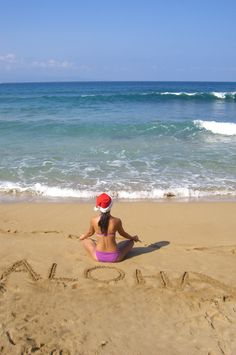 a woman sitting on top of a sandy beach next to the ocean and writing in the sand