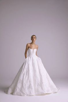 a woman in a white wedding dress standing on a gray background with her hands behind her back