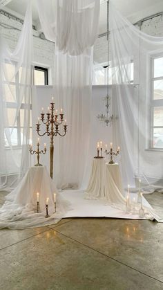 a room filled with lots of white curtains and candles on top of a table next to a chandelier