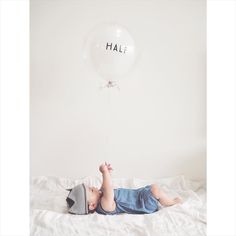 a baby laying on top of a bed under a balloon