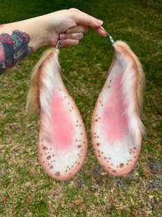 two pink and white furry animal tails being held by a person's hand in the grass