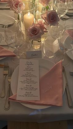 the table is set with silverware and pink napkins, candles and flowers in glass vases