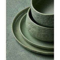 three green dishes stacked on top of each other in front of a white plate and bowl