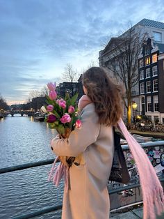 a woman holding flowers on the side of a bridge over water with buildings in the background