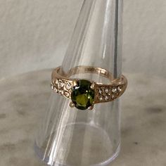 a gold ring with a green stone in the middle and white diamonds around it on a clear glass stand