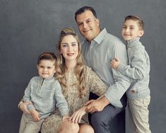 a family poses for a photo in front of a gray background with their two children