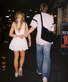 a man and woman walking down the street at night with their back to each other