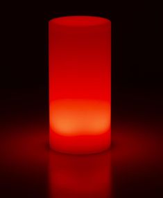 a lit candle sitting on top of a red table next to a black wall and floor