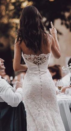 a woman in a white wedding dress standing next to a man at a dinner table