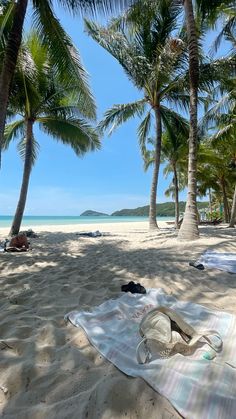 a towel, hat and flip flops are laying on the beach under palm trees