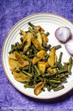 a white plate topped with green beans and potatoes next to an onion on a purple cloth