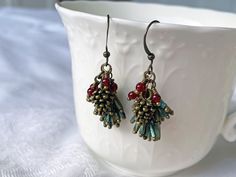 "Pretty little brass pinecones, red glass bead berries, and a spray of iridescent green bugle bead pine needles hang from oxidized brass ear wires.    Length from the top of the ear wire to the bottom of the \"pine needles\" is about 1.5\". Your earrings will arrive nicely packaged in a recycled kraft paper box." Pinecone Earrings Diy, Nature-inspired Beaded Dangle Earrings As Gift, Pine Needle Jewelry, Resin Pinecone Jewelry, Real Pinecone Earrings, Pinecone Earrings, Pine Cone Earrings, Needle Earrings, Jewelry Rustic