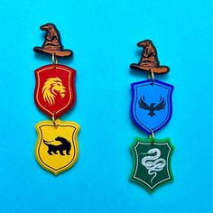 three harry potter inspired earrings on a blue and green background, one with a hogwart's crest