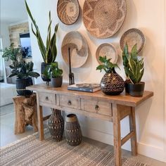 a wooden table topped with potted plants next to a wall covered in wicker baskets