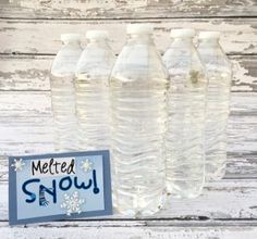 four bottled water bottles sitting on top of a white wooden table next to a sign