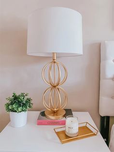 a white table with a lamp and some books on it next to a potted plant