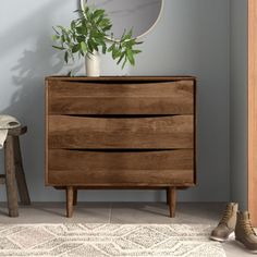 a wooden dresser sitting on top of a white rug next to a chair and potted plant