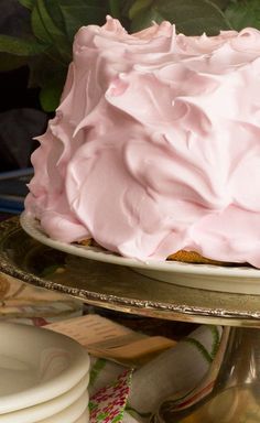 a cake with pink frosting sitting on top of a metal platter next to plates