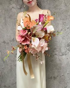 a woman in a white dress holding a bouquet of pink and orange flowers on her shoulder