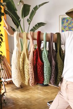 a man standing next to a rack with crocheted bags hanging from it