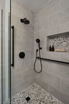 a walk in shower sitting next to a tiled wall and floor with black fixtures on it