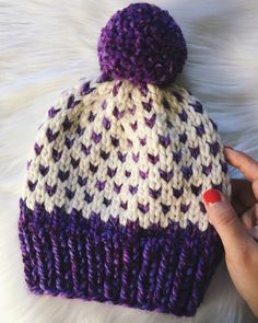 a woman's hand holding onto a purple and white knitted beanie hat