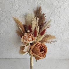 an arrangement of dried flowers and feathers in a vase on a white wallpapered surface