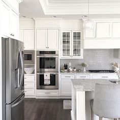 a white kitchen with stainless steel appliances and marble counter tops, along with stools